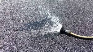 A hose sprays water onto porous asphalt